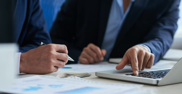 Dois empresários revisando documentos fiscais no notebook para garantir a conformidade fiscal da empresa